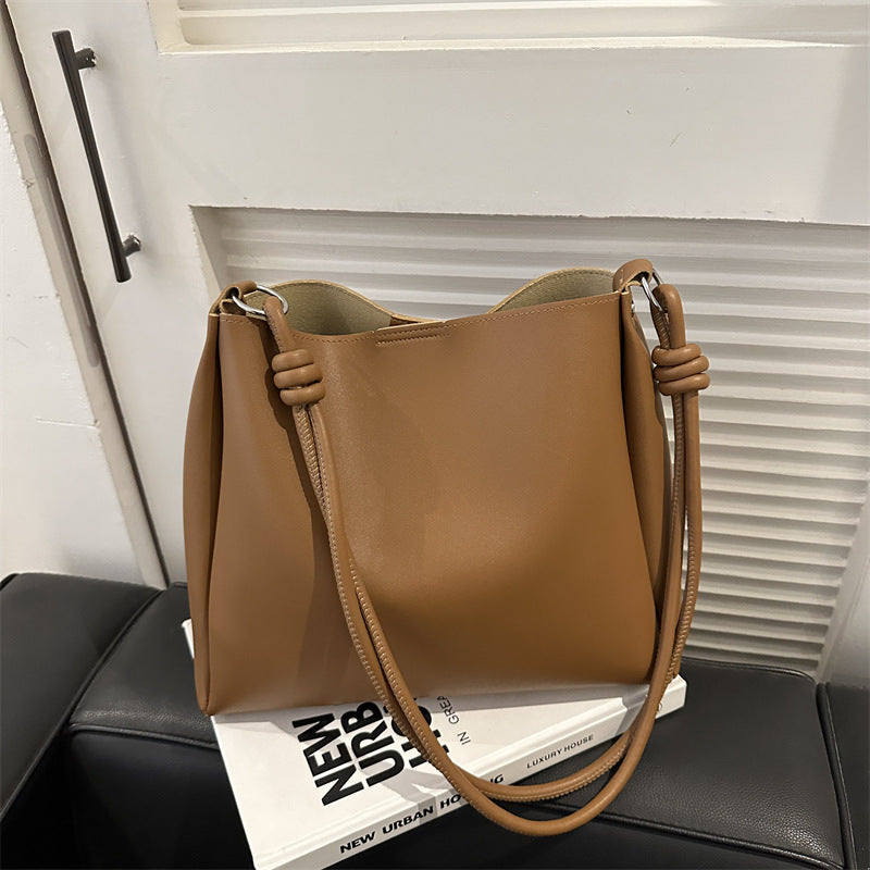 Women's PU leather retro bucket crossbody tote bag in a neutral tone, shown from a side angle highlighting the strap and stru