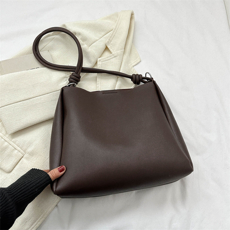Women's PU leather retro bucket crossbody tote bag in a neutral tone, shown from a side angle highlighting the strap and stru